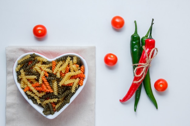 Massa fusilli em uma tigela com pimentos, tomates vista superior na mesa de toalha de mesa branca e dobrada