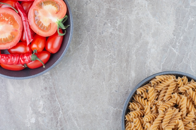 Massas cruas com tomate cereja e pimenta em uma panela preta