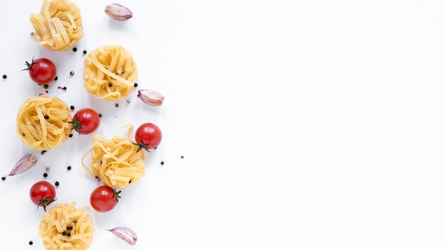 Massas tagliatelle não cozidas; tomate cereja; dente de alho; pimenta preta isolada sobre o fundo branco com espaço para o texto
