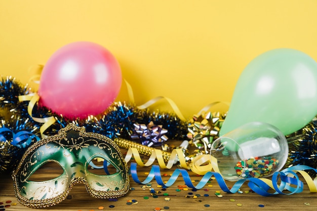 Material de decoração de festa com máscara de penas de carnaval de máscaras e balões na mesa de madeira