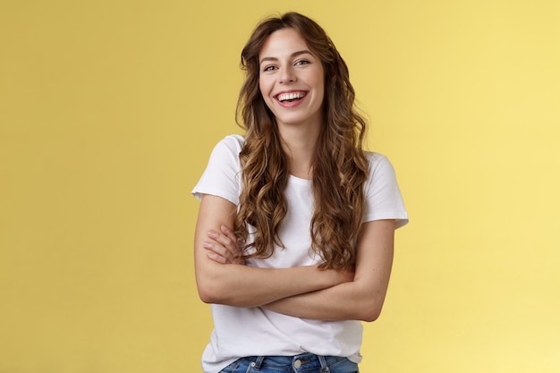 Me divirta. amigável carismático corte de cabelo encaracolado feminino rindo com alegria sair amigos braços cruzados no peito sentir frio ligeiramente frio tem fundo amarelo divertido conversa agradável.