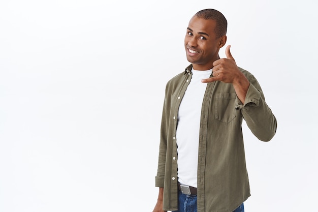 Foto grátis me ligue qualquer hora. retrato de homem afro-americano confiante e atrevido. mostra o sinal do telefone perto da cabeça e sorrindo