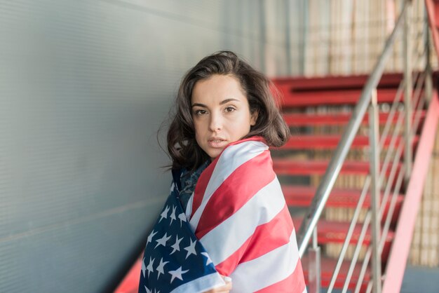 Meados de tiro jovem mulher usando grande bandeira EUA e sentado na escada