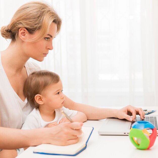 Meados de tiro mãe séria segurando bebê trabalhando na mesa