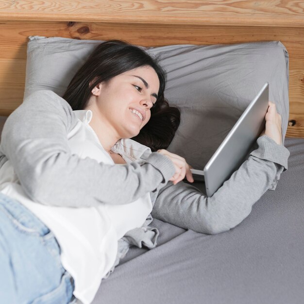 Meados de tiro mulher morena trabalhando em tablet na cama