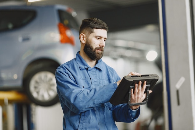 Mecânico de automóveis com um tablet perto de um carro com roupa de trabalho