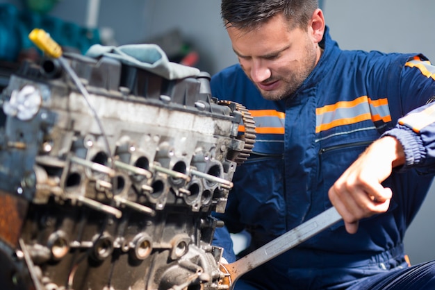 Mecânico de automóveis profissional reparando motor de automóvel usando uma chave inglesa na oficina