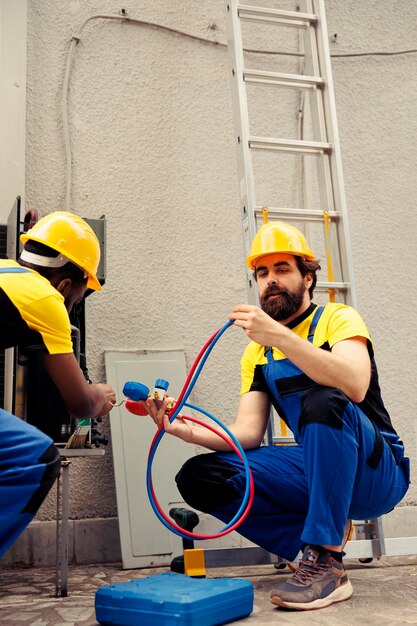 Mecânico experiente usando escova de pó macia para varrer a camada acumulada de sujeira e detritos da bobina do sistema HVAC, enquanto o reparador adepto reabastece o tanque de refrigerante do sistema de resfriamento do ar condicionado