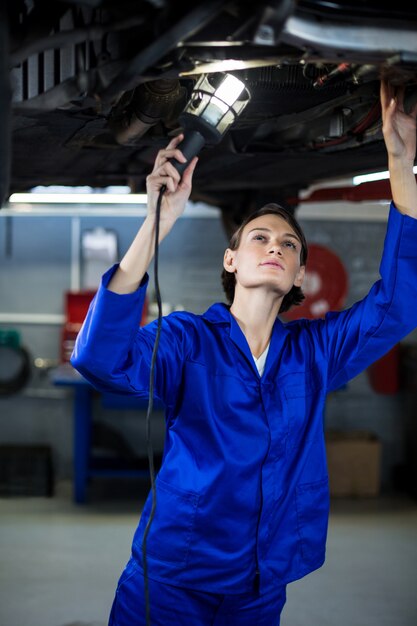 mecânico fêmea que examina um carro com lâmpada