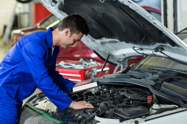 Mecânico que usa a tabuleta digital ao mesmo tempo a manutenção do motor de automóveis