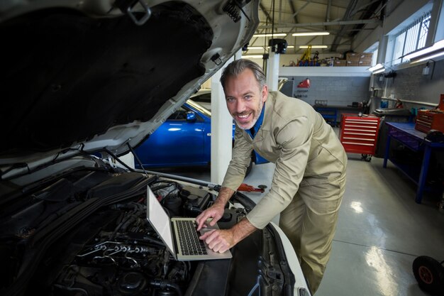 Mecânico que usa o portátil ao serviço um motor de carro