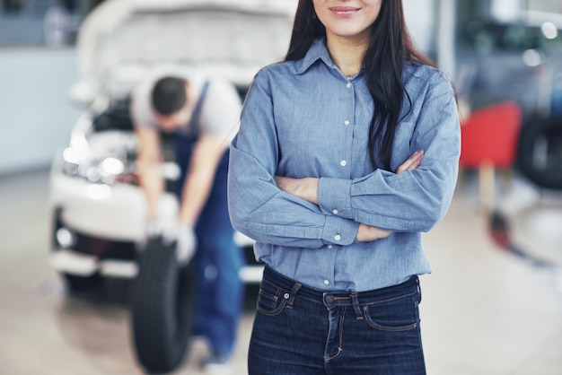 Foto grátis mecânico segurando um pneu na garagem de reparação. a mulher cliente aguarda o trabalho