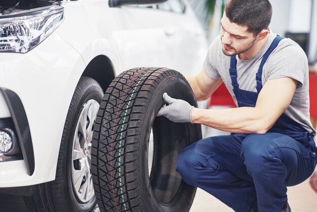 Mecânico segurando um pneu na garagem de reparação. substituição de pneus de inverno e verão
