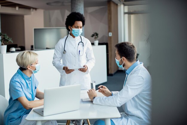 Médica afro-americana conversando com seus colegas enquanto trabalhava na clínica médica durante a pandemia de coronavírus