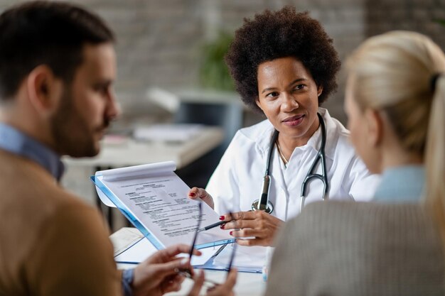 Médica afro-americana mostrando a alguns resultados de teste de seu exame médico na clínica