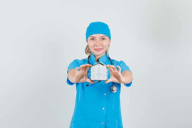 Médica aparecendo modelo de casa e sorrindo com uniforme azul