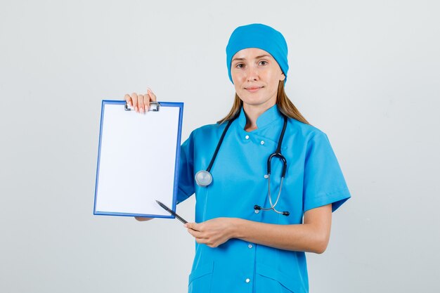 Médica apontando a caneta para a área de transferência de uniforme e parecendo amigável. vista frontal.