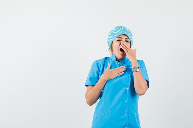 Médica bocejando de uniforme azul e parecendo com sono