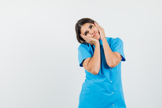 Médica com as mãos nas bochechas com uniforme azul e linda