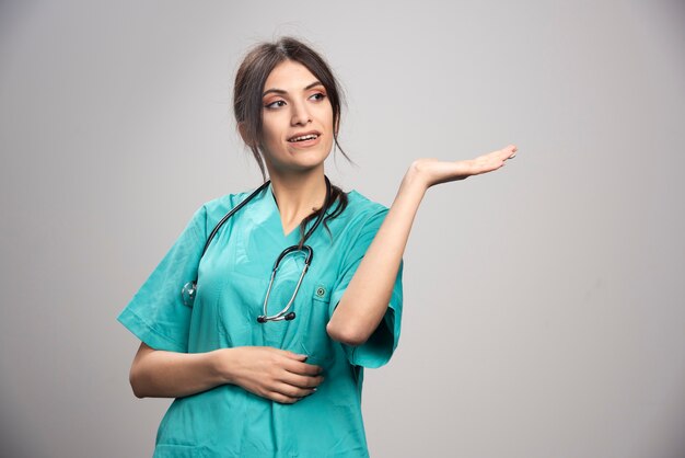 Médica com estetoscópio posando em cinza