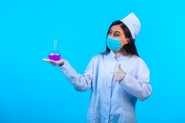 Médica com máscara segurando um frasco de teste e fazendo o polegar para cima