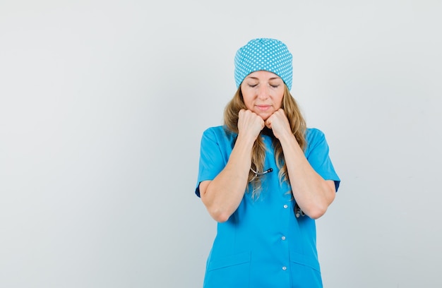 Médica com o rosto apoiado nos punhos em uniforme azul e parecendo estar em paz