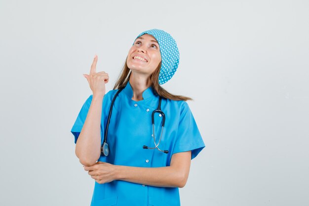 Médica com uniforme azul apontando para cima com gesto de arma e parecendo animada