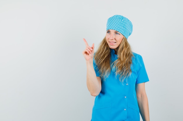 Médica com uniforme azul apontando para cima e parecendo alegre