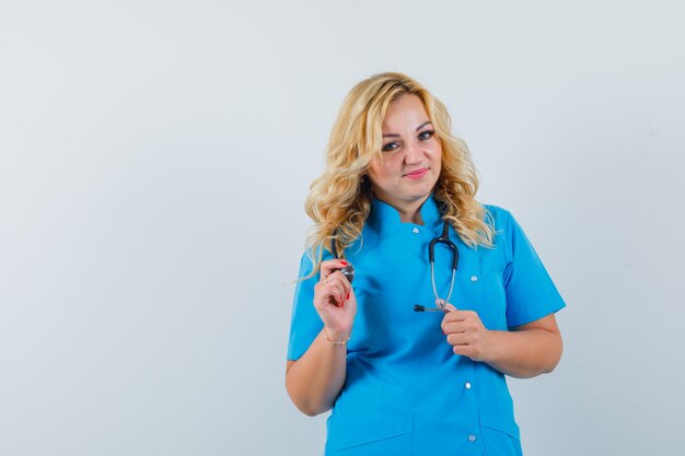 Médica com uniforme azul em pé enquanto segura o estetoscópio e parece confiante