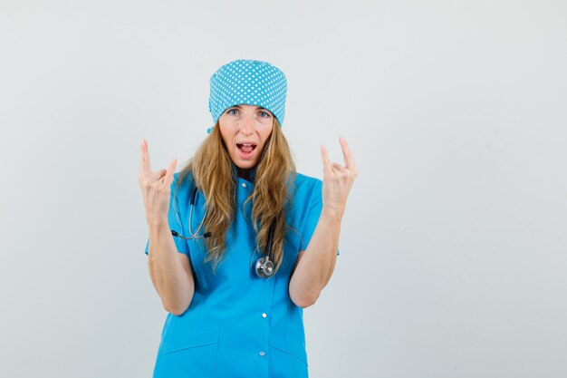 Médica com uniforme azul fazendo o símbolo do rock e parecendo confiante