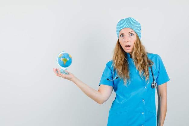 Médica com uniforme azul segurando o globo do mundo e parecendo ansiosa