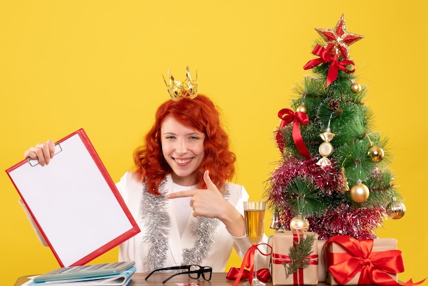 Médica com vista frontal segurando uma nota de arquivo em torno dos presentes de natal e da árvore