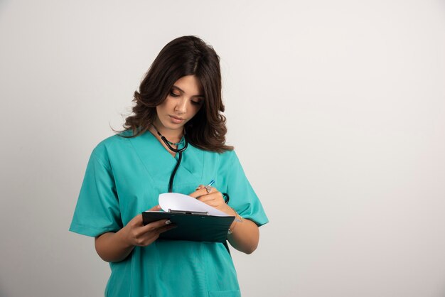 Médica da mulher com estetoscópio lendo notas da área de transferência.