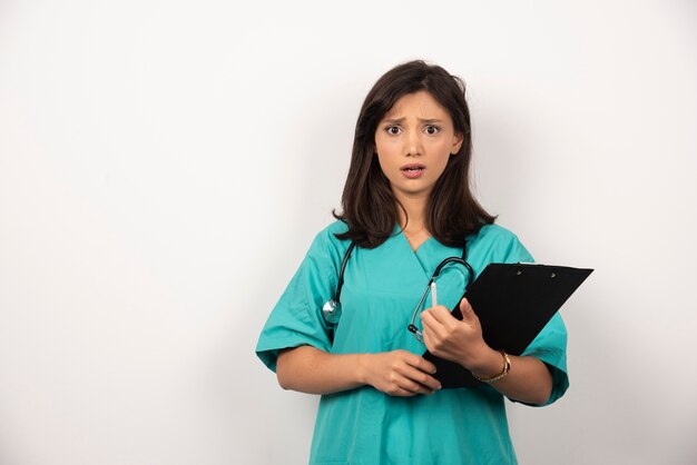 Médica da mulher com estetoscópio segurando a prancheta em fundo branco.