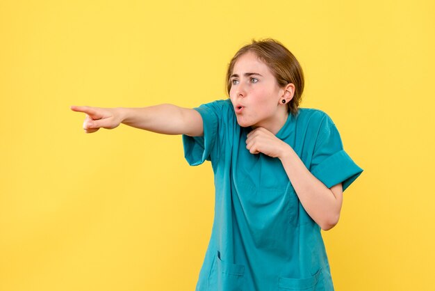 Médica de frente apontando sobre fundo amarelo saúde médico emoções hospital