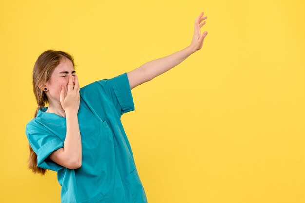 Médica de frente, cobrindo o rosto em um fundo amarelo.