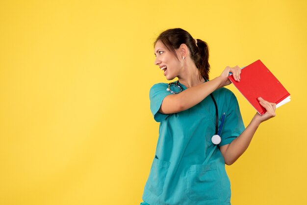 Médica de frente com camisa médica segurando análise sobre fundo amarelo