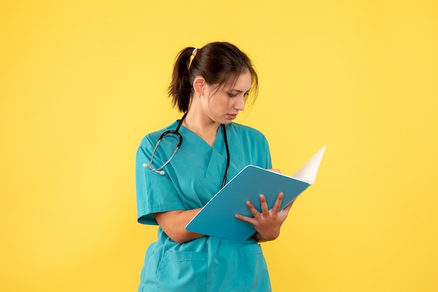 Médica de frente com camisa médica segurando análise sobre fundo amarelo