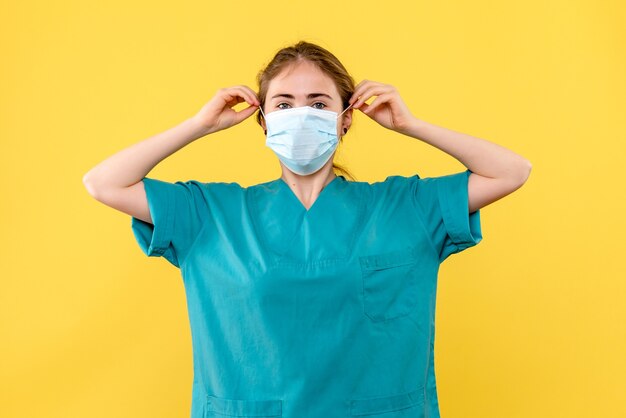 Foto grátis médica de frente com máscara estéril sobre fundo amarelo, vírus pandêmico da saúde covid