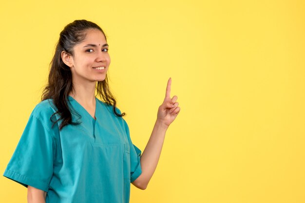 Médica de frente de uniforme apontando para o pé do teto