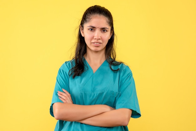 Médica de frente em uniforme, cruzando as mãos em pé