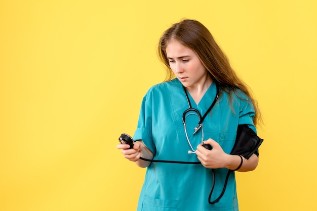 Médica de frente medindo pressão sobre fundo amarelo hospital médico