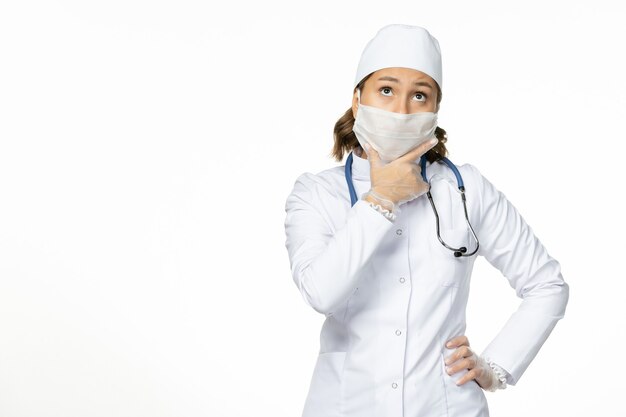 Médica de frente para o terno branco e máscara devido ao coronavírus pensando na doença do vírus pandêmico da parede branca covida