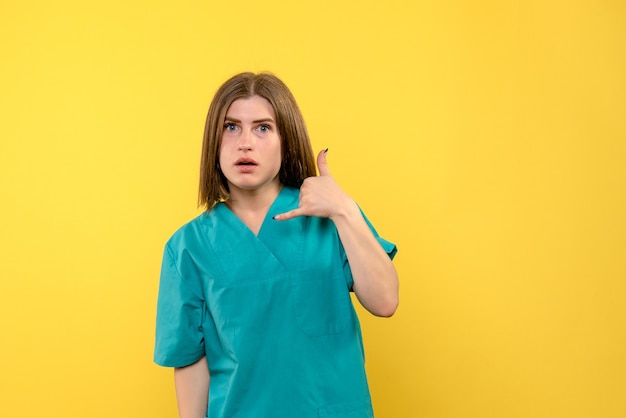 Médica de frente posando em um espaço amarelo claro