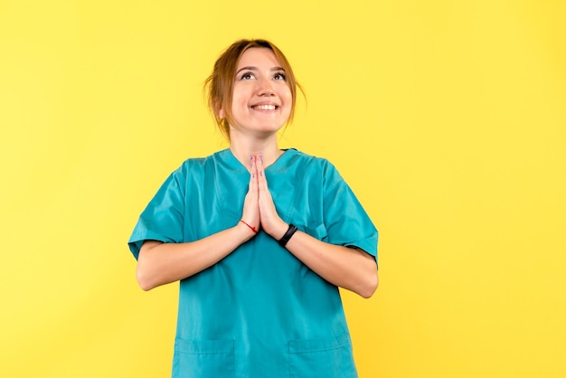 Médica de frente rezando com um sorriso no espaço amarelo