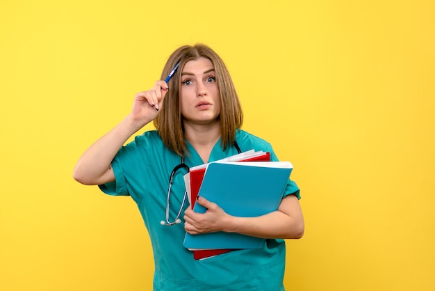 Médica de frente segurando documentos no espaço amarelo