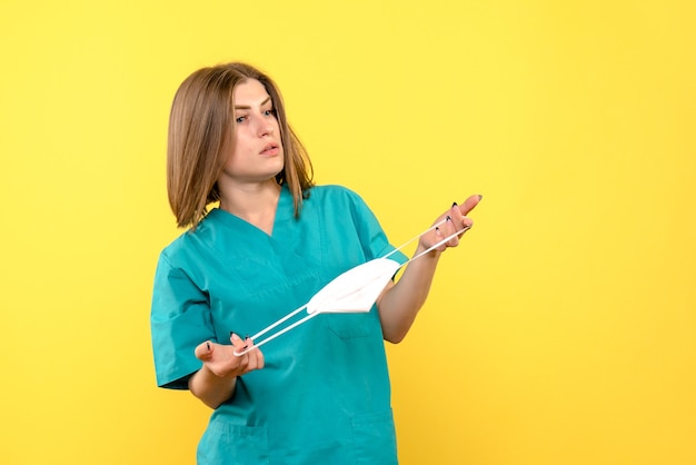 Médica de frente segurando máscara no espaço amarelo