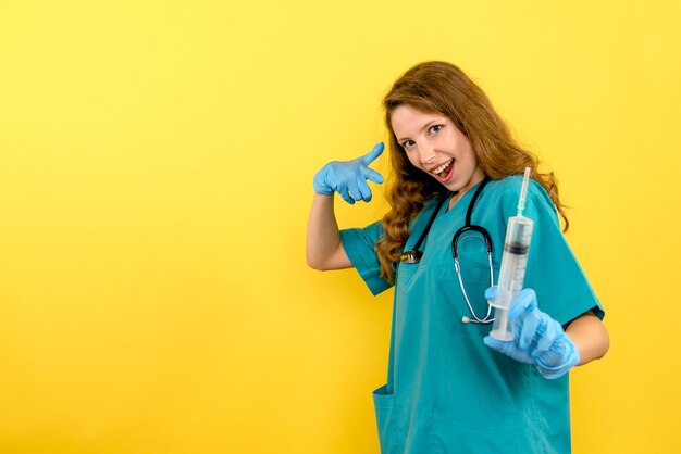 Médica de frente segurando uma enorme injeção no espaço amarelo