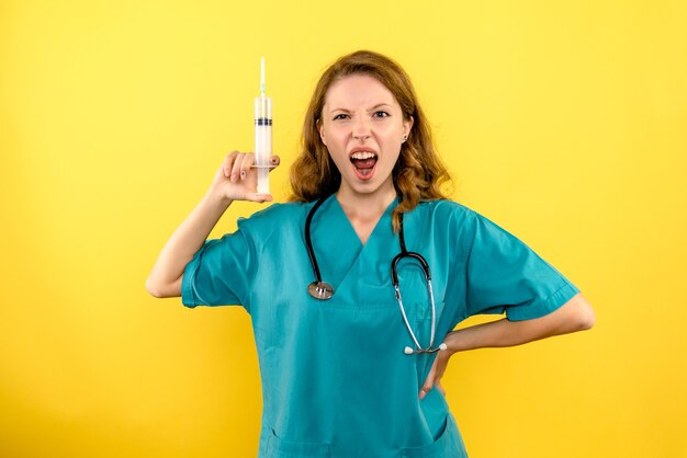 Médica de frente segurando uma grande injeção no espaço amarelo