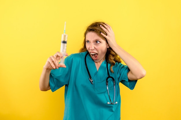 Médica de frente segurando uma grande injeção no espaço amarelo